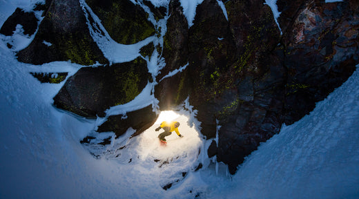 Snowboarder Josh Dirksen rides through a backlit hole in a rock wall